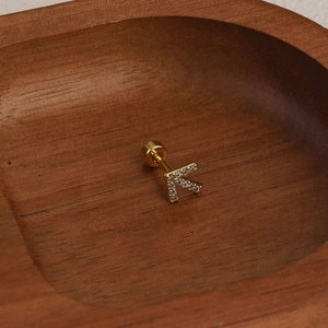 Detailed view of gold K letter stud earring with zircon inlay and screw-back on wood