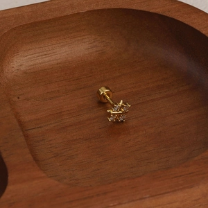 Detailed view of golden flower cartilage stud with white zircon on dark wood tray