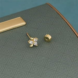 Macro view of gold flower earrings with four clear zircons on green leather
