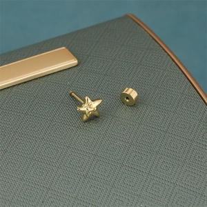 Close-up of gold star earrings with 18K plating and secure screw backs on textured green