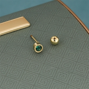 Macro detail of gold-plated stud earring with sparkling green zircon and screw-back closure