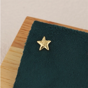 Detailed view of gold star stud earring with a face relief on a green suede pad
