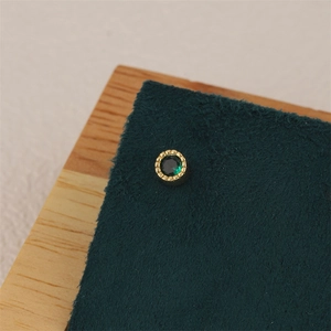 Close-up of a 18K gold plated earring with a green zircon and granular vintage edge
