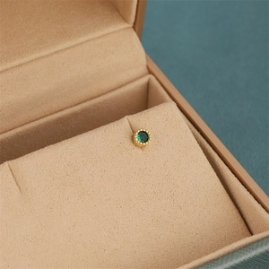 Macro view of gold plated round stud earring with green zircon and millgrain detail
