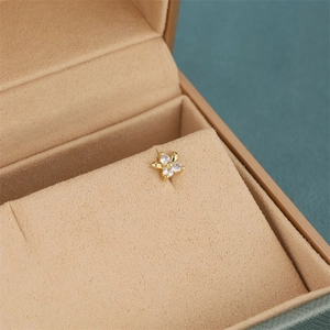 Close-up of gold flower stud earring with four zircons in a beige velvet jewelry box