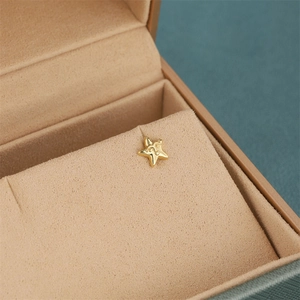 Macro shot of gold-plated star stud earrings featuring a delicate human face engraving