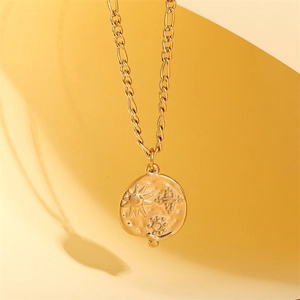 Golden sun medallion necklace with geometric sun relief and Figaro chain on warm background