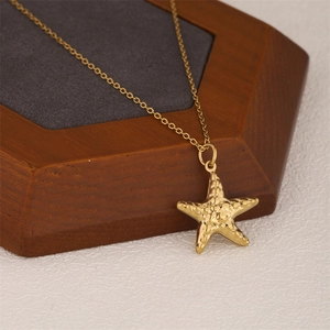 Minimalist gold starfish pendant necklace with textured finish on a wooden jewelry box