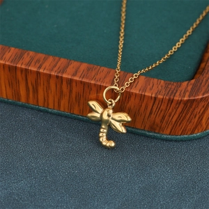 Elegant gold-plated dragonfly pendant necklace in stainless steel on a textured background