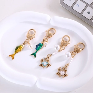 Porte-clés créatures marines dorés avec boucles cœur et perles dans un plat blanc