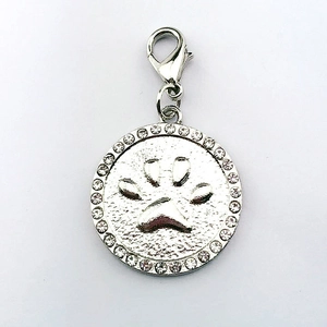 Close-up of a round silver pet tag with rhinestone border and embossed paw print design