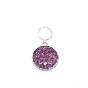 Macro detail of round zinc alloy pet ID tag with purple glitter and cat face outline