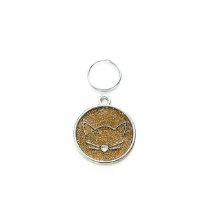 Close-up of circular pet tag with gold glitter, cat silhouette, and heart crystal detail