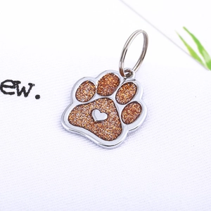 Macro shot of silver pet ID tag with orange glitter paw print and heart detail