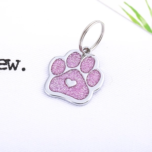 Detail of paw-shaped metal pet ID tag with pink glitter finish and silver heart charm