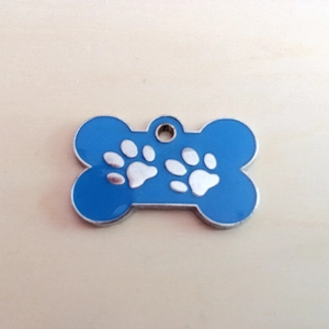 Detail of bone-shaped pet ID tag in blue enamel with silver paw print patterns