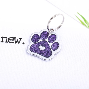 Macro shot of silver metal paw print pet ID tag with purple glitter and heart detail