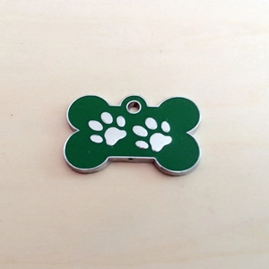 Detailed top view of bone-shaped green enamel dog tag with silver paw prints on wood