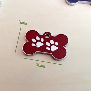 Detail of red bone-shaped dog tag with white paw prints on light wood background