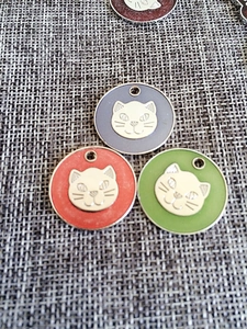 Macro detail of round enamel cat-shaped pet ID tags in grey, orange and green colors
