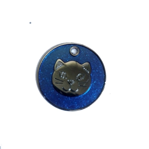 Detail of round metal pet tag with blue glitter base and golden cat head relief icon