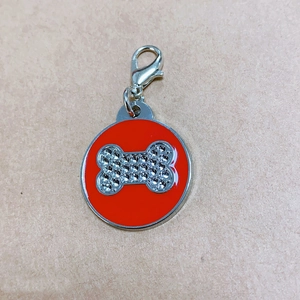 Red enamel pet ID tag with rhinestone bone pattern and metal lobster clasp on beige base