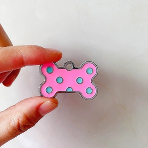 Medaglietta per animali rosa a forma di osso con pois blu e bordo in metallo nella mano