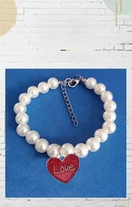 Detail view of pet pearl necklace with red glitter heart pendant and Love engraving
