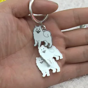 Detail van drie witte emaille hondenhangers aan een zilveren metalen sleutelhanger in de hand