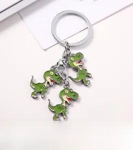 Detail shot of a silver keychain with three green cartoon dinosaur metal pendants on white