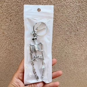 Detailed close-up of a silver skeleton keychain with lobster clasp in a plastic bag