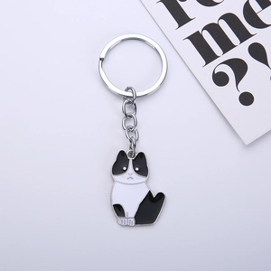 Macro detail of cow-patterned black and white enamel cat keychain with silver metal ring