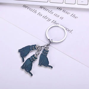 Close-up of three blue enamel cat charms on a silver metal ring with a keyboard background