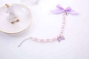 Detail of pink pearl pet collar with purple ribbon bow and rhinestone bone charm