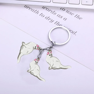 Three white enamel cat charms on a silver alloy keychain over a book and keyboard