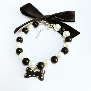Close-up of pearl pet collar featuring black satin bow and rhinestone bone pendant