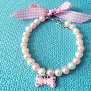 Macro shot of pink pearl pet necklace with checkered bow and rhinestone bone charm