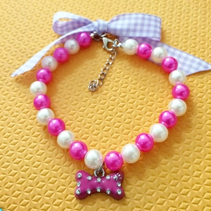 Detail of pink pearl pet necklace featuring purple plaid bow and crystal bone pendant