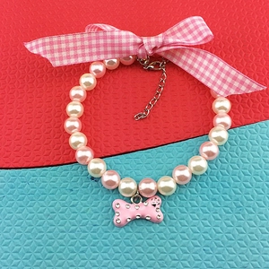 Detailed view of pet pearl necklace with pink bone pendant and checkered ribbon bow