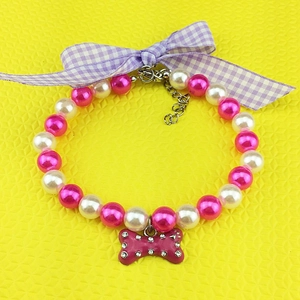 Detail of pink pearl pet necklace with a plaid bow and rhinestone bone pendant