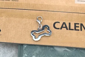 Silver hollow bone-shaped pet charm with lobster clasp on a vintage paper background
