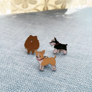 Drei Emaille-Hund-Anstecknadeln mit Pomeranian- und Schnauzer-Motiven auf blauem Stoff