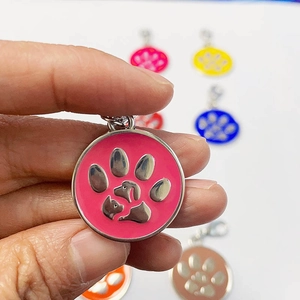 Macro detail of round metal pet ID tag with pink paw print and secure lobster clasp