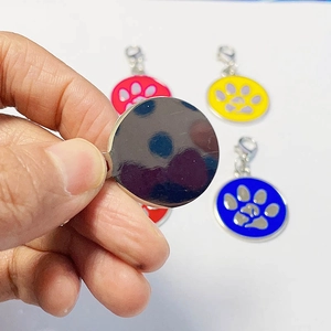 Detail view of round pet ID tag with colorful paw prints and metal back for engraving
