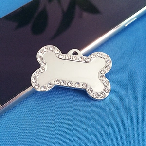 Macro shot of silver bone-shaped pet ID tag with rhinestones on blue knit background