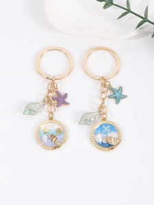 Detail of seashell and starfish pendants on golden metal keychains with ocean sand design