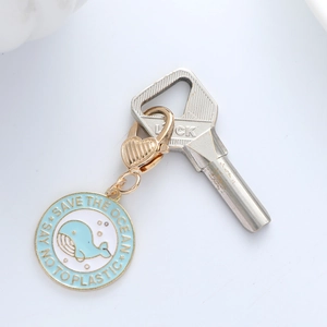 Detail of light blue enamel whale keychain with golden metal trim and heart lobster clasp