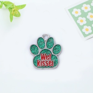 Detail view of a paw-shaped metal pet tag with green glitter and Wet Kisser engraving