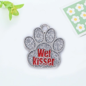 Macro shot of silver paw-shaped pet tag with glitter texture and red Wet Kisser lettering