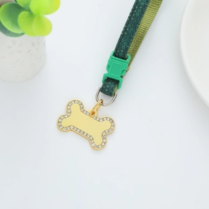 Gold bone-shaped pet tag with rhinestones and green floral collar on white background